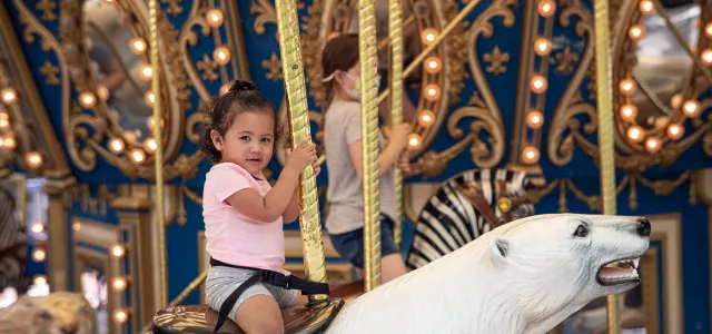 A little girl riding a polar bear on a carousel.