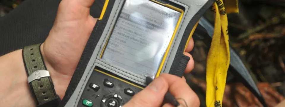 View of someone's hands holding a SMART spacial monitoring and reporting tool, which is a small, black handheld device the size of a cell phone.