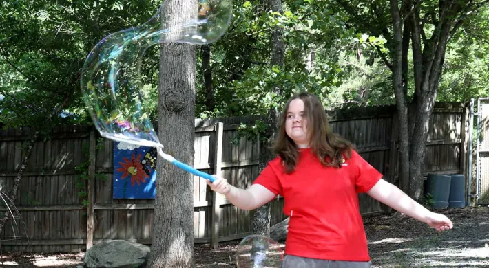 Play Pal teen volunteer moving a bubble wand with a large bubble coming out