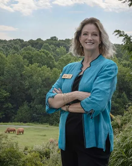 Diane Villa standing in front of a grassy field with two rhinos in the distance