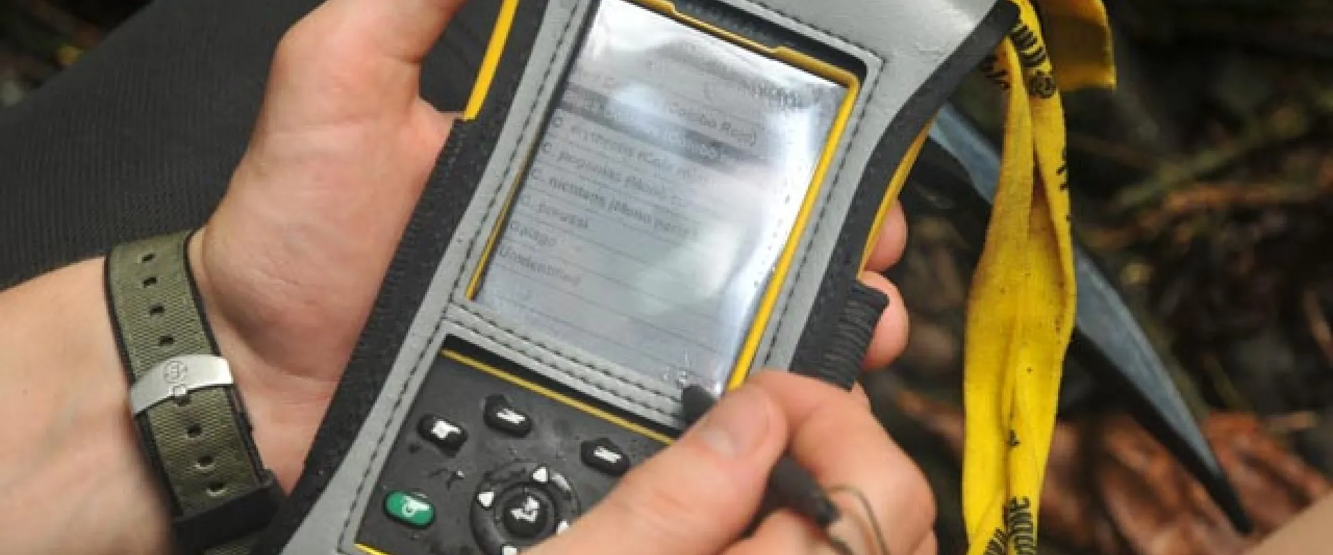 View of someone's hands holding a SMART spacial monitoring and reporting tool, which is a small, black handheld device the size of a cell phone.