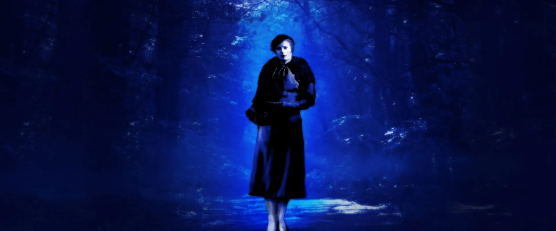 A dark, highly saturated blue, stylized image of a woman standing in a forest. She is illuminated by a bright, almost ethereal blue light from above and is wearing 1940s-style clothing, including a long skirt, a short jacket or shawl, and a small dark hat.