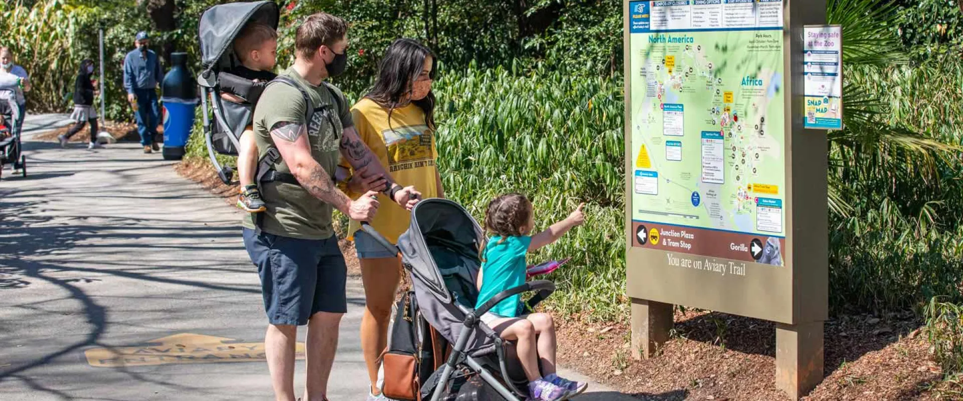 A family, including a child in a stroller and another in a carrier, looks at a map at a zoo.