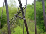 A closeup on a part of a metal art installation that showcases a small, metal dragonfly appearing mid flight in front of some tall cattail stalks. There is a green forest visible in the blurred background.
