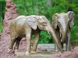A small bronze statue of two Elephants standing together, one reaching its trunk out towards the other. Mounds of mud and a termite mound are placed around them.