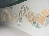 A large painted and textured mural of a Sonoran Snake. The body spans the length of a long, tan wall, and features a colorful desert scene full of native plants and animals.