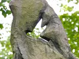 A large stone with the shape of a bird that appears to be in flight carved into the middle of it. A canopy of trees and a clear sky are visible through and around the stone.