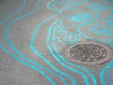 A series of swirly blue lines painted on a concrete path. They flow together to resemble the look and movement of stream water.