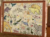  A colorful outdoor mural made of a large grid of painted ceramic tiles depicting various African animals, including a rhino, lion, elephants, zebra, and several birds, set against a background of plants. Flanking the tile mural are two brown panels with white text; the left panel is titled "The Lion's Pride."