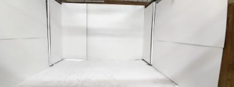  An indoor enclosure for animals is shown with white panels forming the walls and a layer of white paint covering the floor. A red bucket sits in the bottom left corner of the frame. The enclosure appears to be under a metal roof structure.