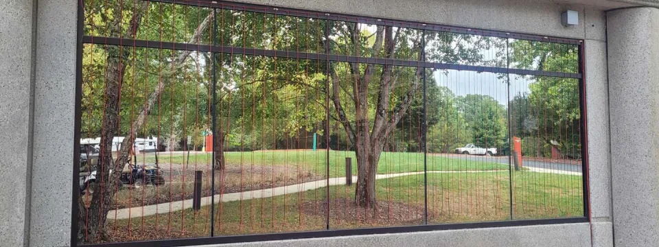 A large, very reflective window on a textured grey building that shows the parking lot across the road.