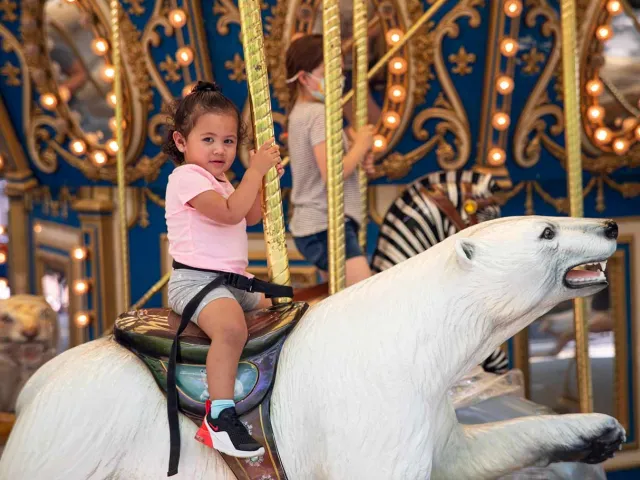 A little girl riding a large polar bear figure on a carousel.