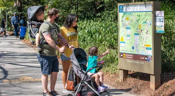  A family, including a child in a stroller and another in a carrier, looks at a map at a zoo.