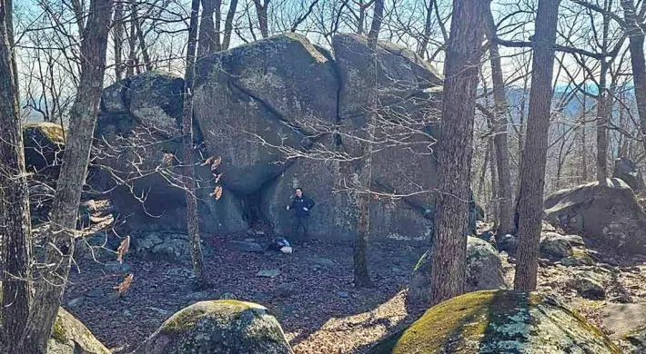  A hiker standing next to an enormous rock on the ridgeline of Ridge's Mountain.
