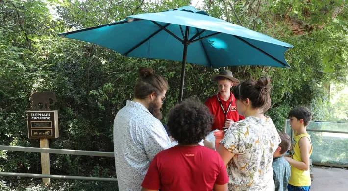A volunteer assisting a diverse family at a Zoo Trekker investigation station.
