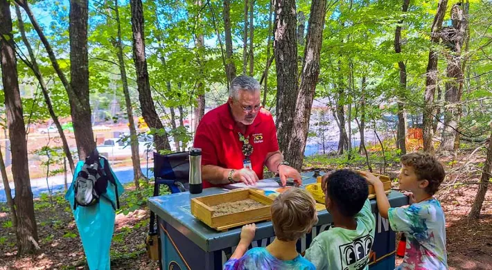 Zoo Volunteer sharing information with three children at a cart on the pathway.