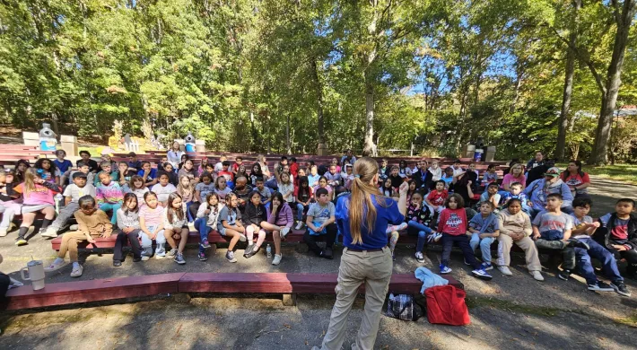 Educator Elizabeth speaks to a large group of kids at an outdoor auditorium. 