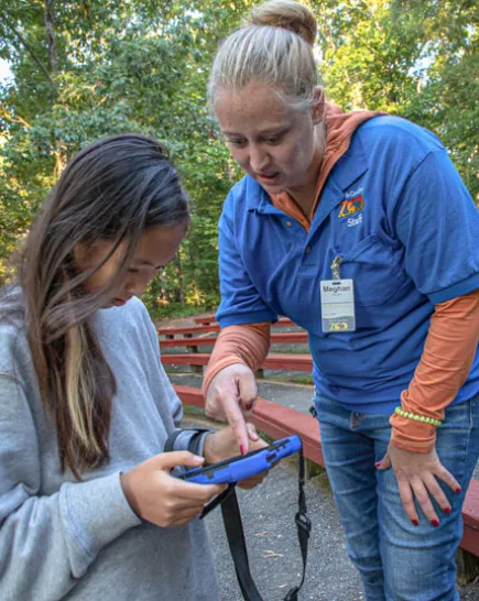 Educator with a young Asian girl showing her how to use a program on a tablet.