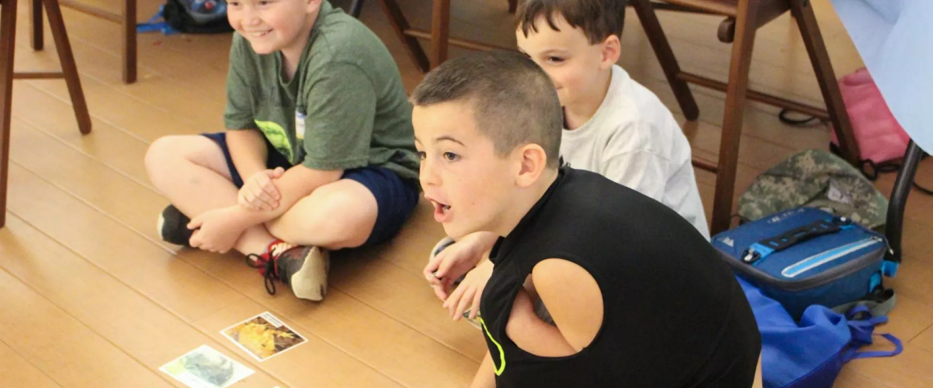 Three young boys grin and make excited gestures during a camp amphibian program.
