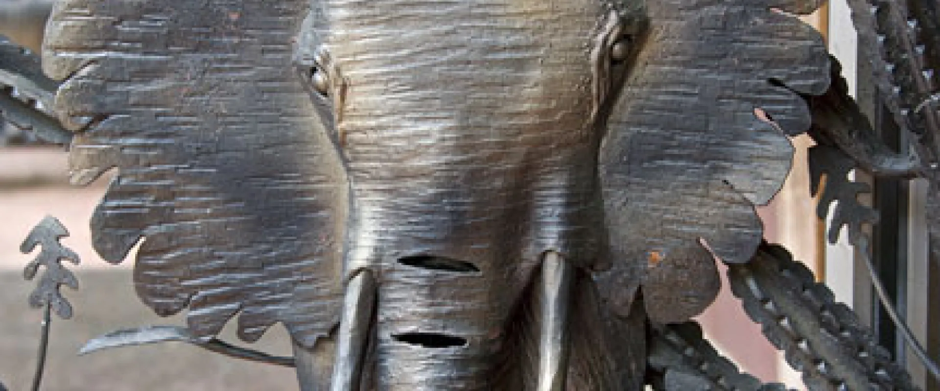 Close-up of a metal elephant design surrounded by other plants and filigree on the larger African Gates.