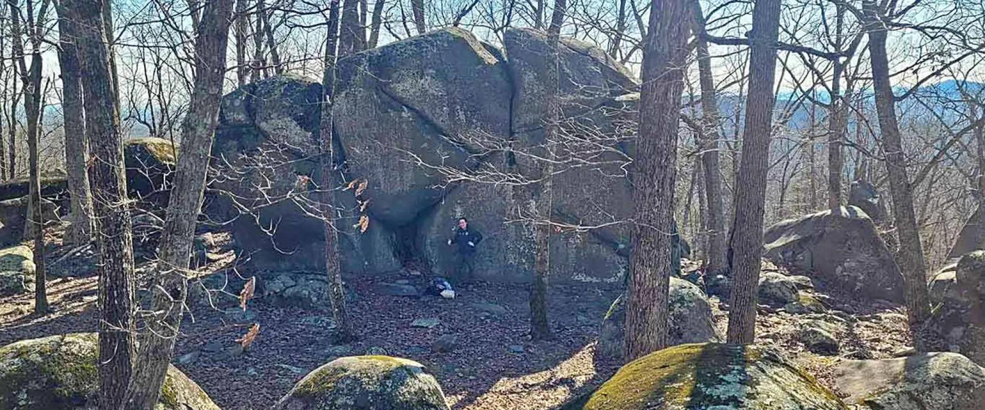  A hiker standing next to an enormous rock on the ridgeline of Ridge's Mountain.