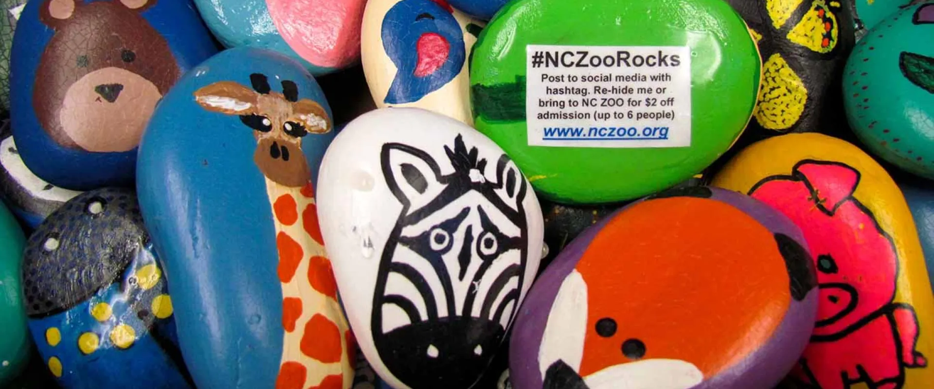 A pile of colorful rocks painted with animals including a zebra, fox, bear, pig and giraffe.