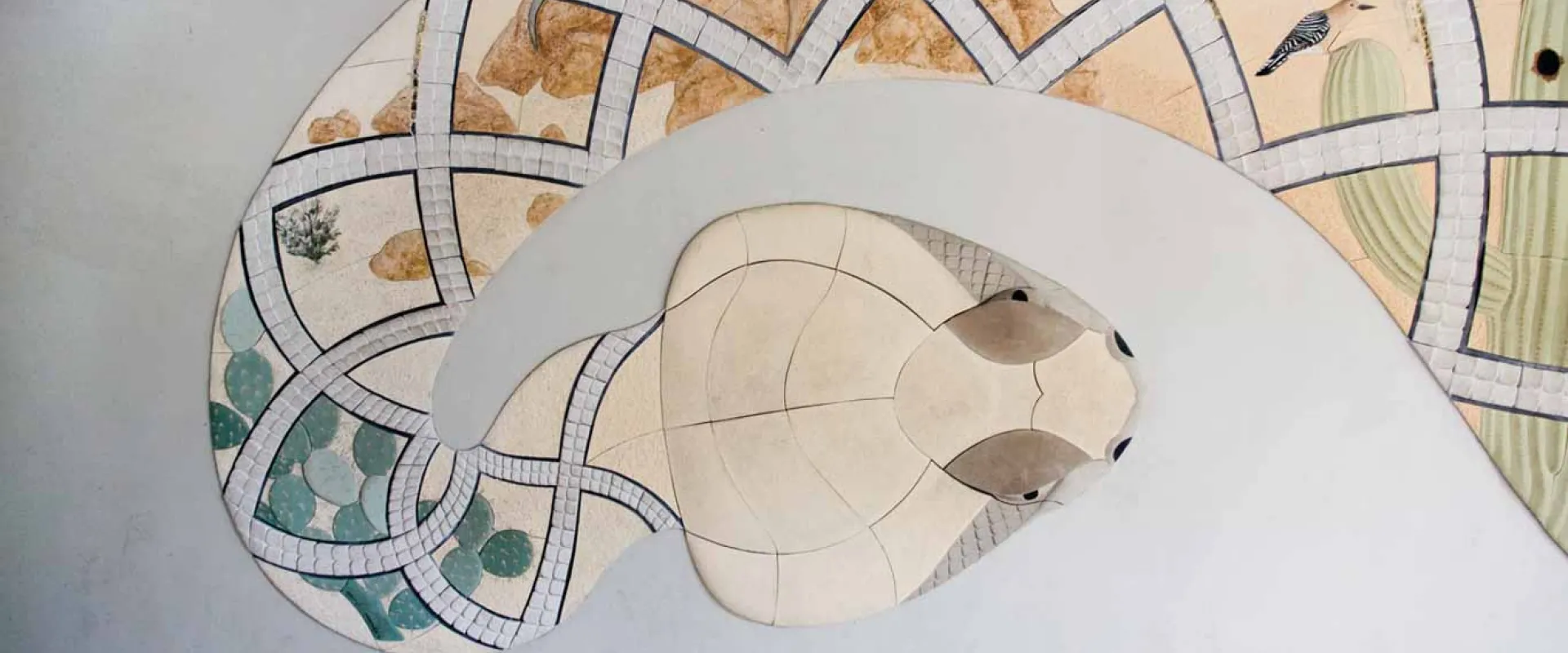 A large textured mural of a Sonoran Snake featuring a colorful design of desert animals and landscape within its scales.