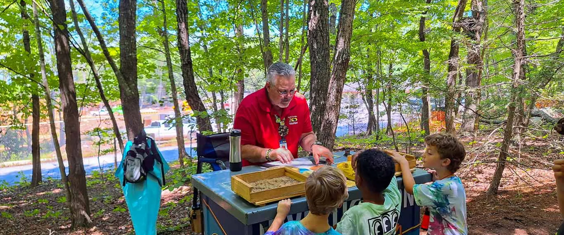 Zoo Volunteer sharing information with three children at a cart on the pathway.