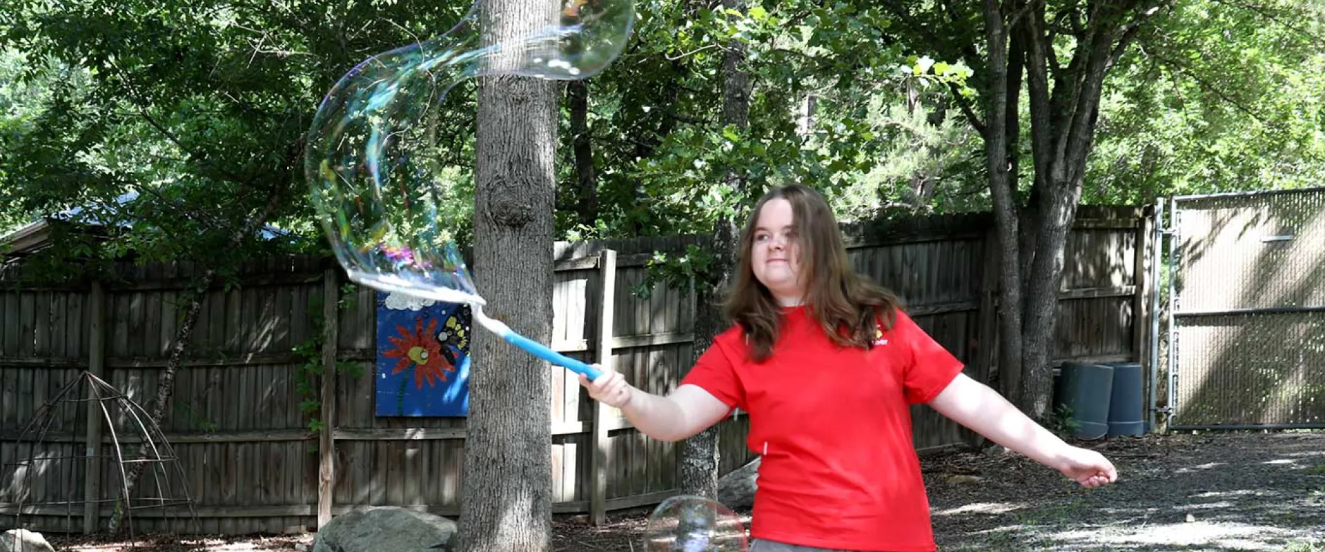 Play Pal teen volunteer moving a bubble wand with a large bubble coming out