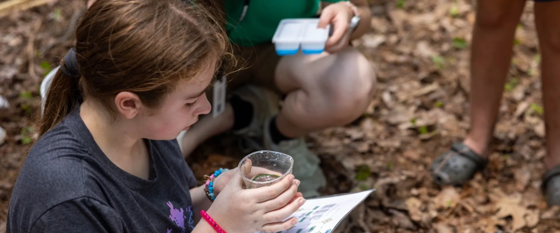 Camper holding a cup with an animal inside, while identifying the animal using a paper chart.