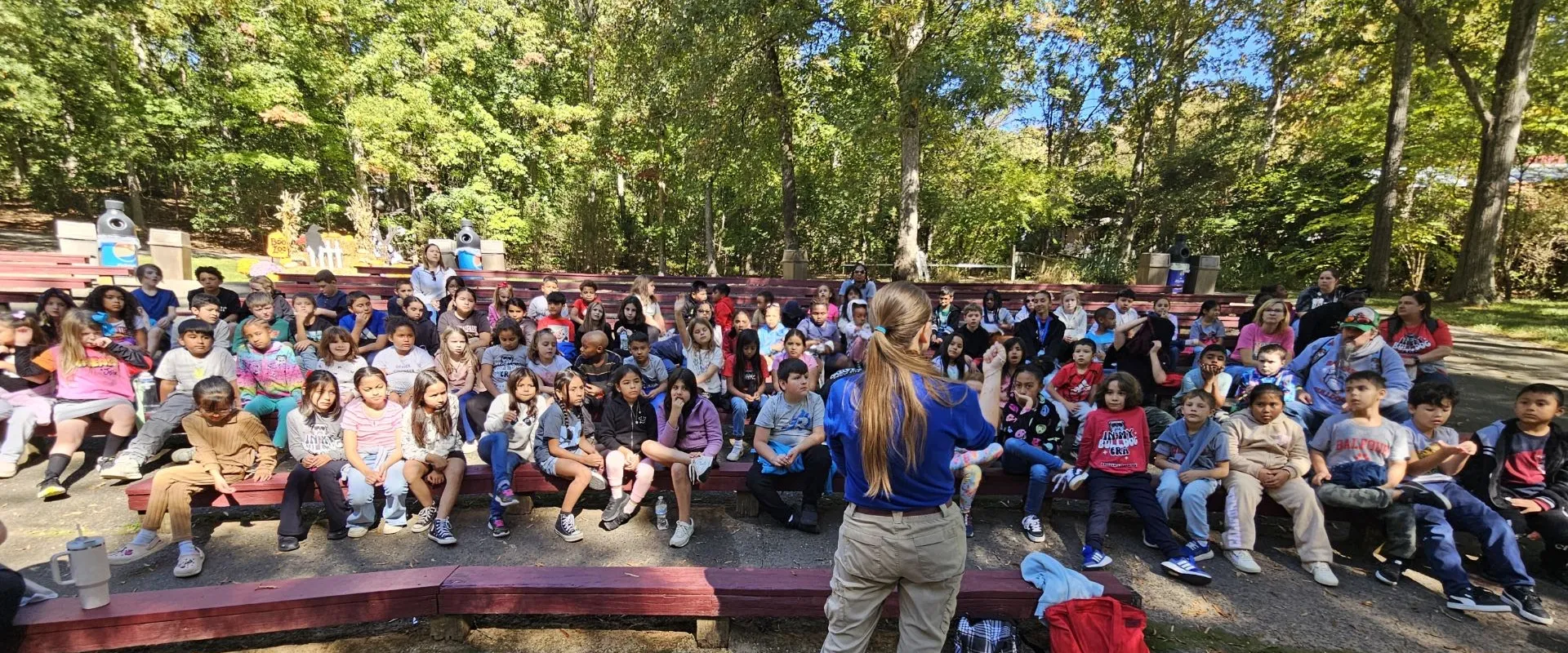 Educator Elizabeth speaks to a large group of kids at an outdoor auditorium.