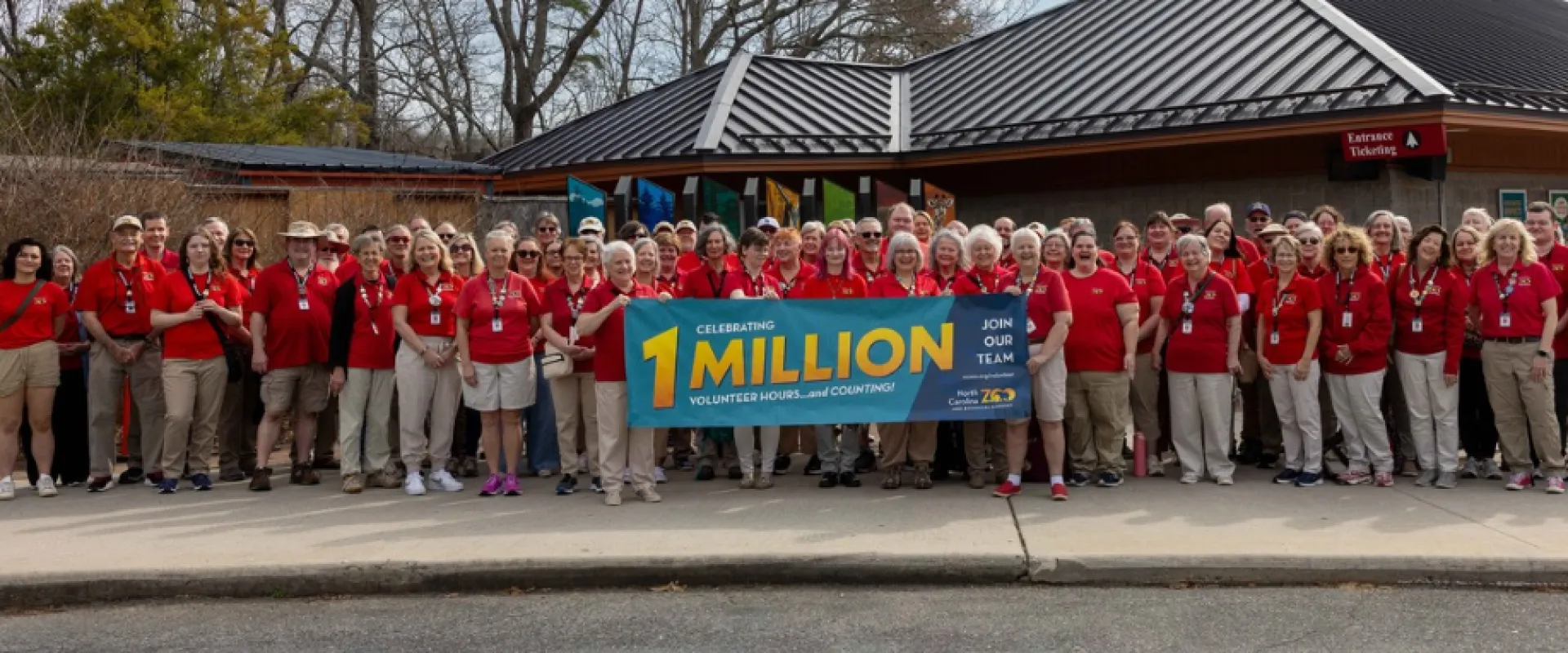 A diverse group of Zoo volunteers stand together in red shirts holding a sign celebrating one million volunteer hours and counting.