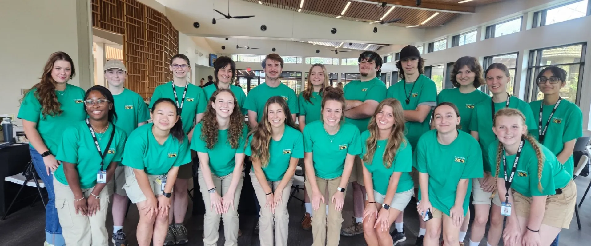 A group photo of Interns at the Zoo inside a building. In the group photo all the interns are wearing matching green shirts.