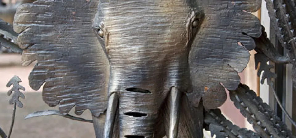 Close-up of a metal elephant design surrounded by other plants and filigree on the larger African Gates.