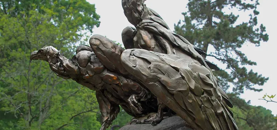 A bronze of three vultures perched close together on a giant boulder, their necks craned and stretched out scanning the wooded area they are in.
