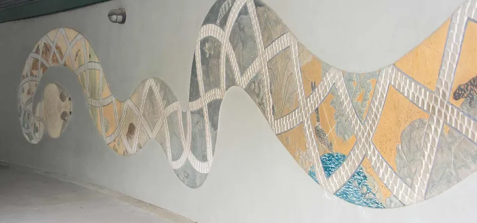 A large painted and textured mural of a Sonoran Snake. The body spans the length of a long, tan wall, and features a colorful desert scene full of native plants and animals.