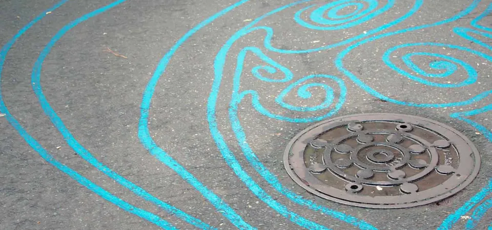 A series of swirly blue lines painted on a concrete path. They flow together to resemble the look and movement of stream water.