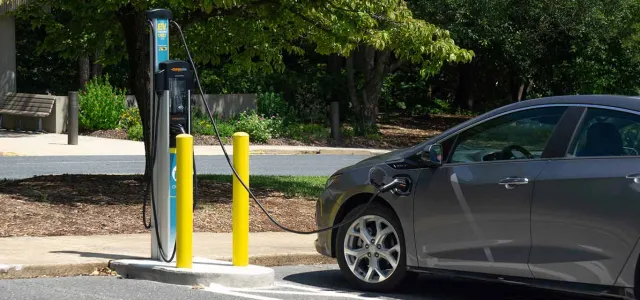 A grey Electric Vehicle parked next to a charging station with a cord, charging at the North Carolina Zoo.