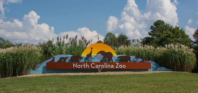 North Carolina Zoo Entrance Sign with animal silhouettes and colorful shapes and sun behind the animals.