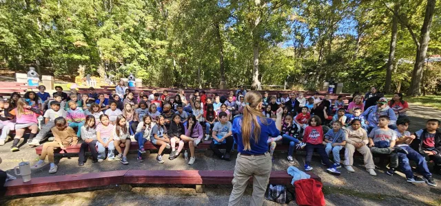 Educator Elizabeth speaks to a large group of kids at an outdoor auditorium. 