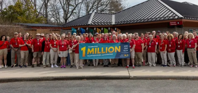 A diverse group of Zoo volunteers stand together in red shirts holding a sign celebrating one million volunteer hours and counting.