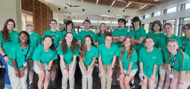 A group photo of Interns at the Zoo inside a building. In the group photo all the interns are wearing matching green shirts. 