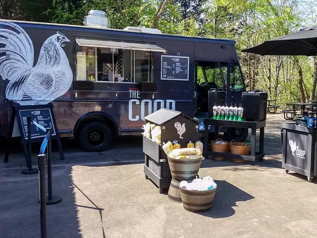 A black food truck with a white rooster logo and words reading "The Coop" is parked in a Plaza at the Zoo.