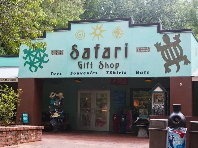 The Safari Gift Shop at the North Carolina Zoo, offering toys, decorative items, and novelties. The building has a light blue facade with brown accents and a sign with animal symbols.