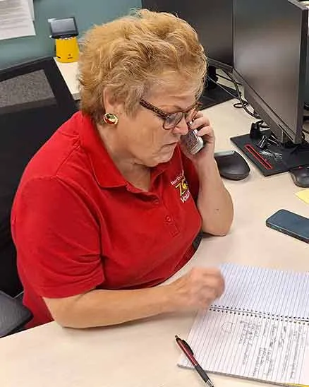 Zoo volunteer sitting at a desk talking on the telephone with a notebook in front of her. 