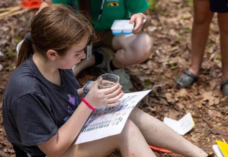 Camper holding a cup with an animal inside, while identifying the animal using a paper chart.