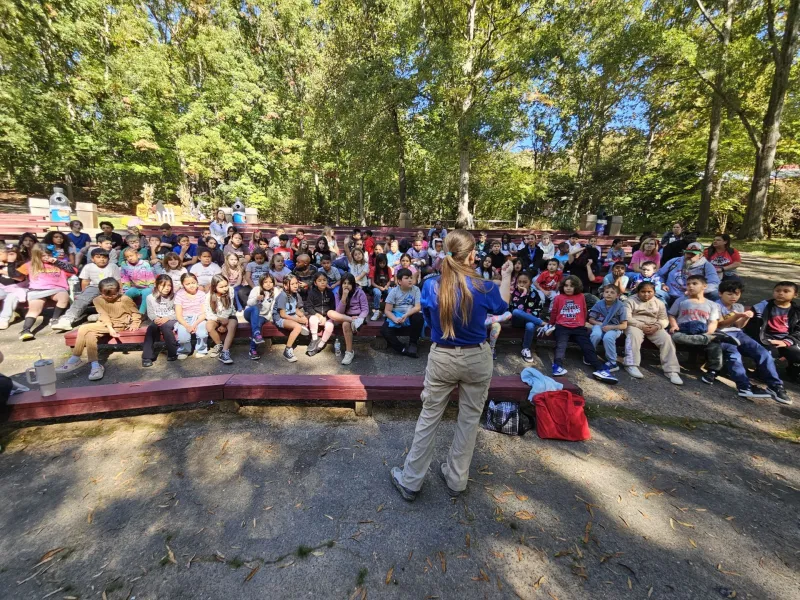 Educator Elizabeth speaks to a large group of kids at an outdoor auditorium.